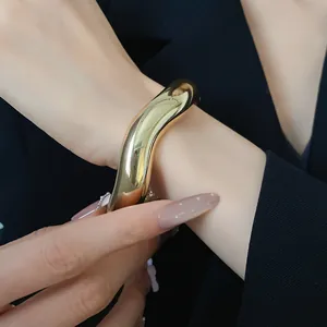 Primo piano di un bracciale a fascia aperta ondulato dorato minimalista su un polso