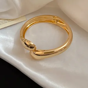 Vista dettagliata dell'elegante bracciale rigido dorato liscio con incrocio a goccia