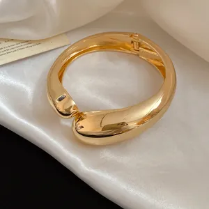 Vista dettagliata del bracciale rigido dorato a goccia incrociata su seta bianca lucida