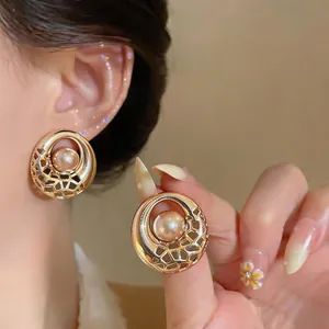 Close-up detail of elegant gold hollow mesh earrings with central pink pearls on ear.