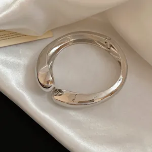 Macro del bracciale rigido a goccia incrociata in metallo lucido con finitura a specchio