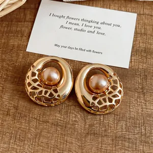 Detailed view of gold hollow-out stud earrings with central champagne pearl inlay