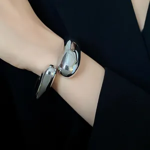 Primo piano di un bracciale rigido minimalista in argento a forma di goccia sul polso.