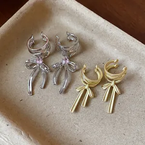 Detail view of silver bow ear cuff with pink zircon and matte gold bow ear cuff.