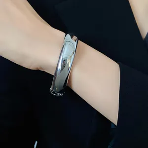 Dettaglio di un bracciale rigido aperto in metallo argentato lucido minimalista