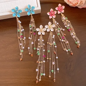 Vue détaillée de boucles d'oreilles vintage en émail avec pompons, perles et chaînes dorées