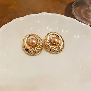 Detailed view of gold-tone hollowed-out stud earrings with pearl center