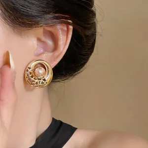Detailed close-up showing the intricate hollow gold design of circular pearl stud earrings