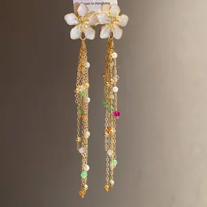 Gros plan de boucles d'oreilles à pompons dorés avec fleurs en émail blanc et perles colorées