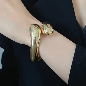 Primo piano di un bracciale rigido dorato a goccia con texture lisce e martellate al polso.