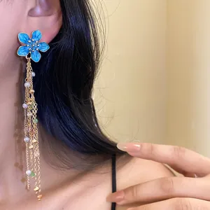 Vue détaillée d'élégantes boucles d'oreilles fleur émail bleu avec perles et chaînes dorées.