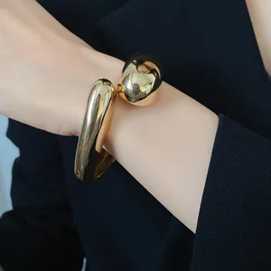 Dettaglio di un bracciale rigido dorato minimalista con design a goccia incrociata