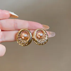 Close-up of golden hollow round stud earrings with center champagne pearl