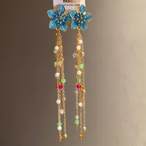 Détail de boucles d'oreilles fleurs en émail bleu avec glands dorés et perles colorées