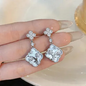 Close-up of elegant silver drop earrings with mother-of-pearl and flower zircons