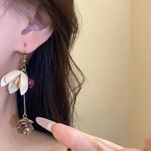 Detail view of handmade vintage earring with cream flower and pinecone pendant
