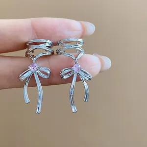 Close-up of elegant silver bow ear clips with sparkling pink zircon stones held by fingers