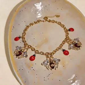 Vintage gold necklace with crystal bee and red ladybug charms on a decorative plate