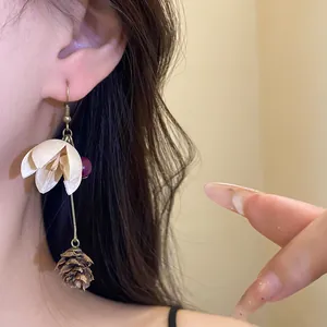 Close-up of vintage style drop earrings featuring a dried pine cone and white flower.