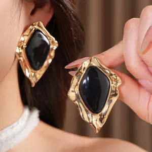 Close-up of irregular textured gold earrings with glossy black enamel center worn on ear