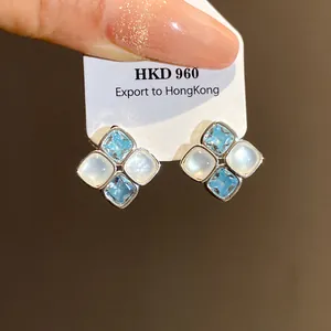 Close-up of diamond-shaped silver stud earrings with light blue zircon and white resin