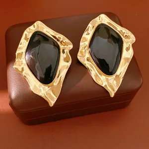 Detailed macro shot of irregular gold-tone and black enamel stud earrings on leather box