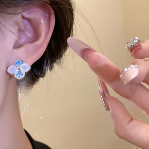 Detail showing iridescent blue and white square stud earrings worn on ear