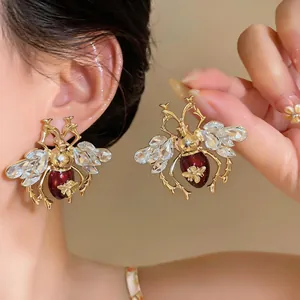 Exquisite close-up of vintage style gold bee earrings with red enamel and crystals