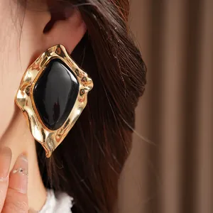 Close-up view of chunky gold irregular geometric earrings with black enamel center