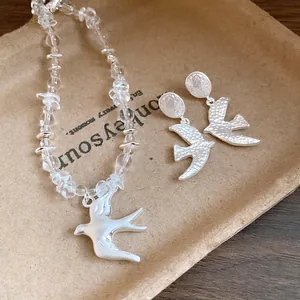 Detailed view of crystal bead necklace and earrings with matte silver swallow pendants