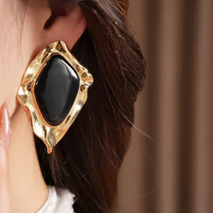 Detailed close-up of irregular geometric gold-tone earrings with glossy black enamel
