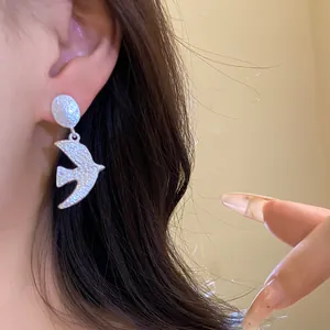 Close-up view of a minimalist silver brushed swallow pendant earring worn on the ear