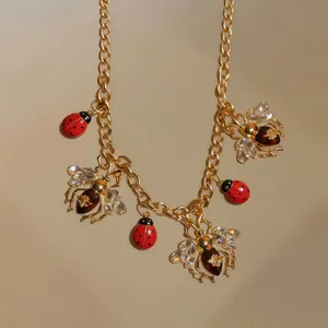 Close-up of vintage gold charm necklace featuring red ladybugs and crystal bees