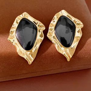 Close-up of geometric irregular earrings with black enamel center and gold-tone textured metal