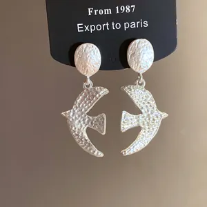Detailed view of brushed silver swallow bird pendant earrings on a black display card