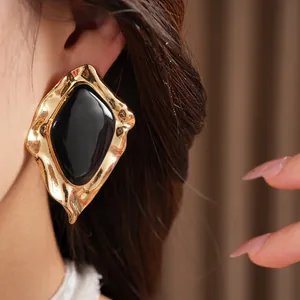 Close-up detail shot of geometric irregular gold earrings with black enamel drip oil center