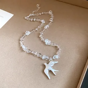 Detailed shot of clear crystal beads and a brushed silver swallow bird pendant necklace