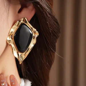 Close-up detail of oversized gold irregular earring with a sleek black enamel center.