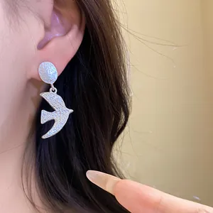 Detailed macro shot of a minimalist brushed silver swallow pendant earring worn on ear.