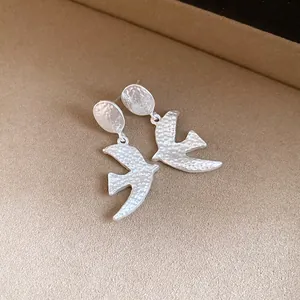 Close-up detail of silver-toned textured swallow-shaped drop earrings for women