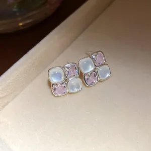 Close-up of elegant square stud earrings with pink zircon and white resin on a beige tray.