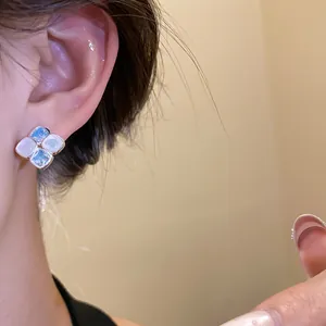 Detailed view of square stud earrings featuring blue zircon and white resin on an ear.