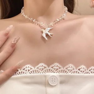 Close-up detail of clear crystal beads and a brushed silver swallow pendant necklace