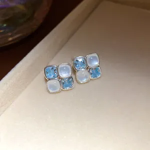Macro detail view of square stud earrings with blue zircon and white resin stones.