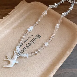 Close-up of minimalist crystal beaded necklace with a swallow pendant on a brown tray