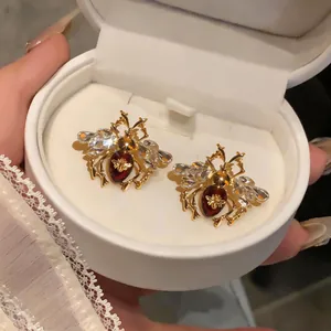 Close-up detail of vintage bee stud earrings with crystal wings and reddish oil-drop body.