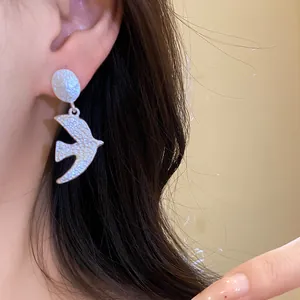 Detailed macro view of a brushed silver swallow pendant earring worn by a model