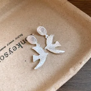 Close-up of matte silver swallow bird drop earrings with hammered texture