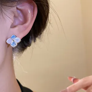 Elegant silver needle stud earrings with blue and white resin stones worn on ear.
