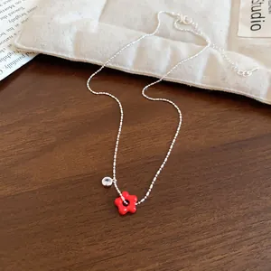 Detailed view of silver beaded necklace featuring a red enamel flower and clear zircon charm